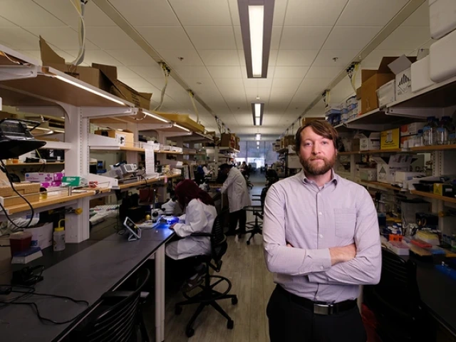 Philip Gutruf stands in his laboratory with researchers working in the background.